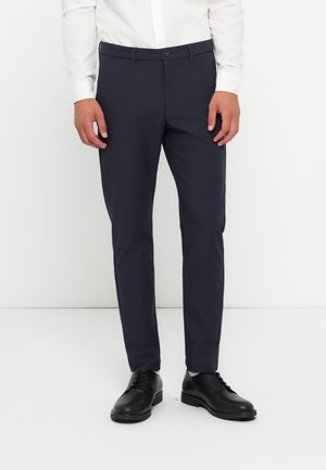 Navy slim-fit trousers made of smooth fabric, featuring a flat front, belt loops, and a single-button closure. Worn with black leather shoes.