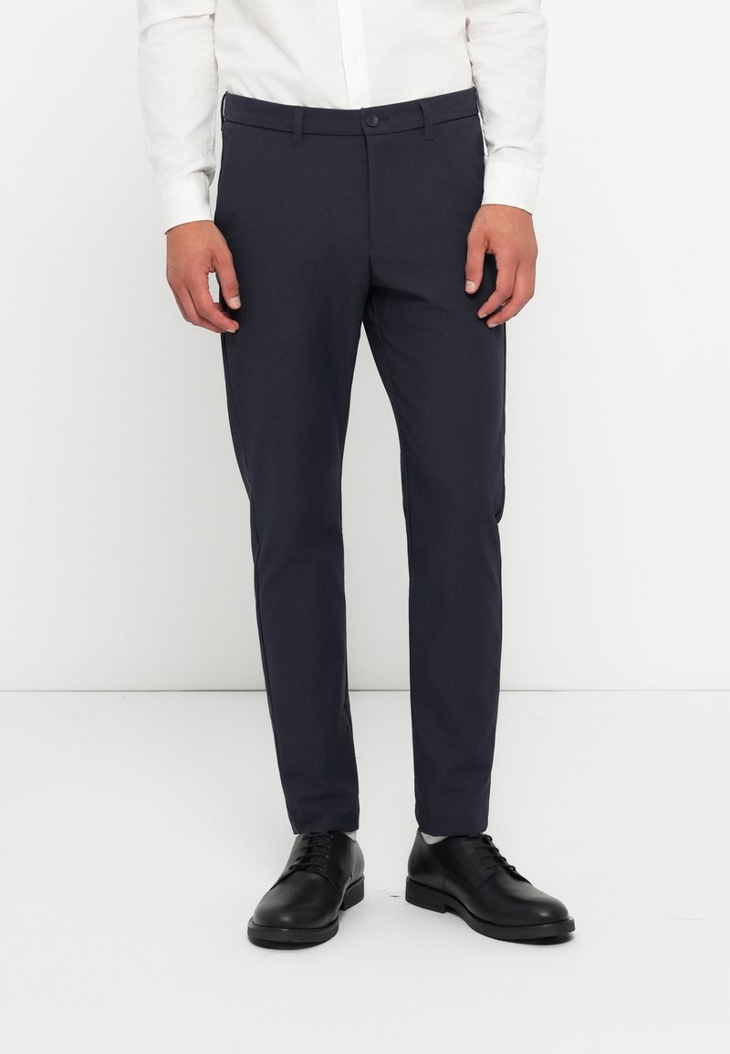 Pantaloni slim-fit navy dintr-un material neted, cu față plată, bucle pentru curea și închidere cu un singur nasture. Purtați cu pantofi din piele negri.