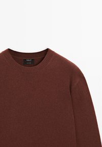 Brauner Rundhalsausschnitt-Pullover aus weichem Stoff, mit geripptem Kragen und glatter Textur, versehen mit einem angenähten Etikett am Kragen.