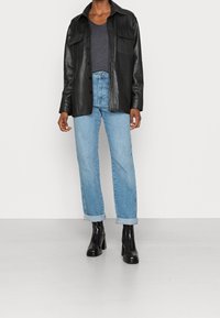 Veste-chemise en cuir noir avec deux poches, associée à un jean droit bleu clair aux revers retroussés et des bottines noires à talons.