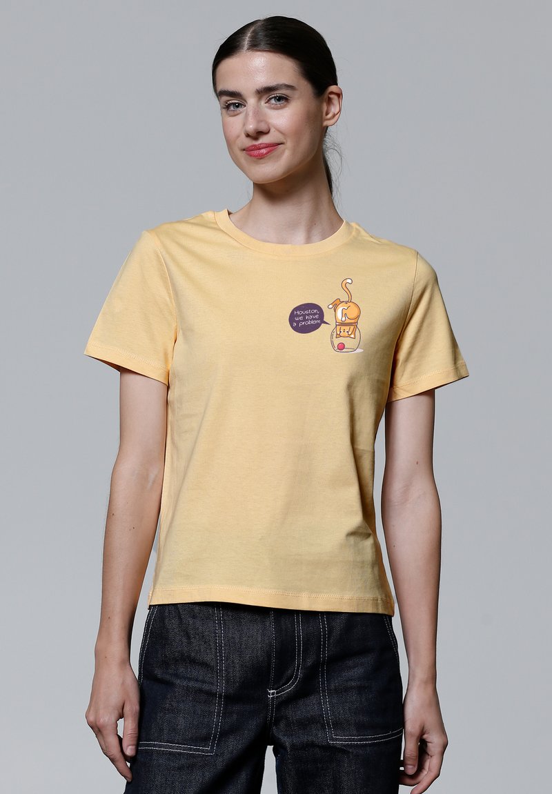 Gelbes Baumwoll-T-Shirt mit Rundhals, kurzen Ärmeln, mit einem Cartoon-Design und Text auf der Vorderseite. Getragen mit dunklen Jeans.