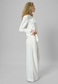 Weiße Satinbluse mit langen Ärmeln und Knopfdetails, kombiniert mit weitem weißen Hosen. Glatte Textur, taillierter Schnitt, minimalistisches Design.