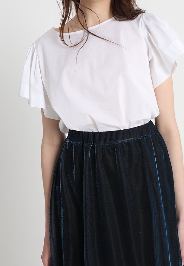 Vit kortärmad topp med volangaxlar, kombinerad med en lång, mörkblå, glänsande plisserad kjol. Mjuk tygtextur och elastisk midja.