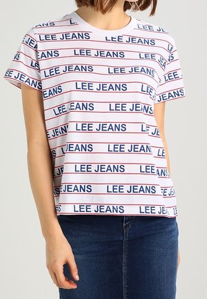 Vrouw draagt een wit T-shirt met horizontale rode strepen en herhaalde "LEE JEANS" tekst in blauw, gecombineerd met donkerblauwe jeans.