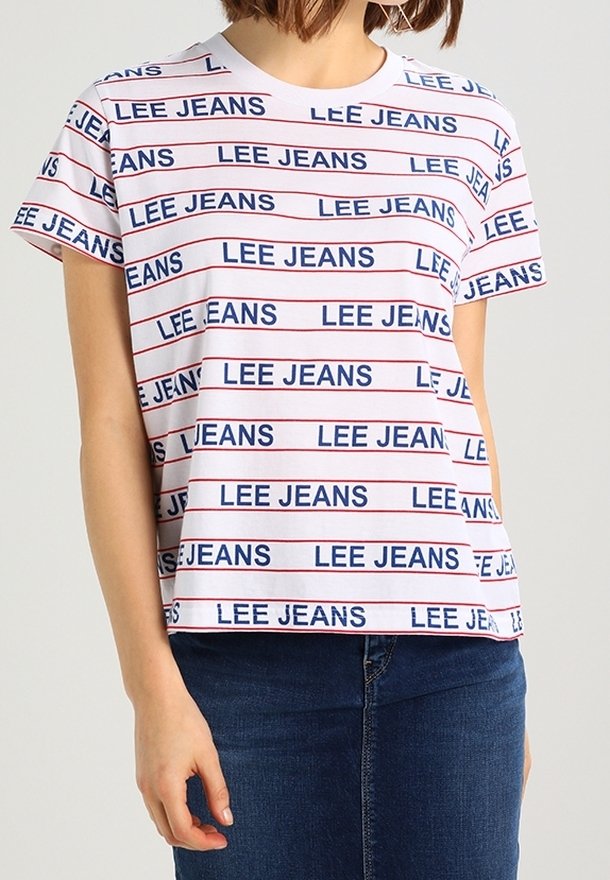 Femme portant un T-shirt blanc à rayures horizontales rouges avec le texte répété "LEE JEANS" en bleu, associé à un jean bleu foncé.
