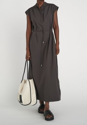 Personne portant une robe midi sans manches de couleur foncée avec une ceinture à la taille, portant un grand sac fourre-tout crème, et des sandales noires à enfiler.
