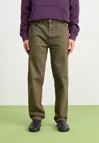Dark green denim jeans with a relaxed fit, featuring five pockets and subtle fading, paired with a purple hooded sweatshirt and black shoes.