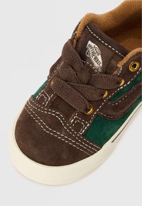 Pruunid ja rohelised sametised Vans jooksujalatsid valgete õmblustega, pruunide paeltega, kuldsete silmadega ja valge kummist tallaga, vaadatuna ülevalt.