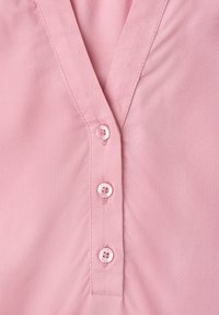 Devant de chemise rose clair avec encolure en V et trois petits boutons ronds fixés verticalement au centre.