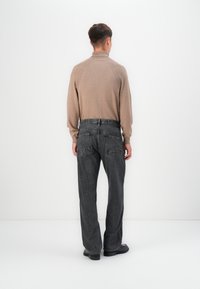 Grijze jeans met achterzakken, gedragen met een lichtbruine gebreide trui met ribbelstructuur. Slim-fit ontwerp, zachte textuur en casual stijl.