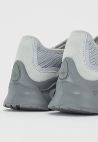 Baskets grises en mélange de daim et de mesh, avec un talon texturé, une semelle rembourrée et un accent de logo à l'arrière.