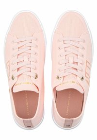 Zapatillas de lona rosa claro con un diseño de malla transpirable, suelas de goma blancas, ojales dorados y detalles de marca en el interior.