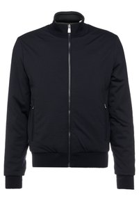 Giacca nera con zip, caratterizzata da un colletto alto, polsini a costine, tasche laterali e una trama liscia. Design minimalista, senza motivi o accenti visibili.