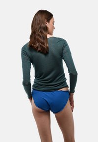 Chemise verte à manches longues avec une coupe ajustée, associée à un short bleu à volants. Texture du tissu douce visible, avec un accent sur le contraste des couleurs.