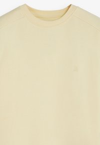 Sudadera de cuello redondo de color amarillo claro, hecha de tejido texturizado. Presenta un sutil acento de logo en el área del pecho izquierdo.