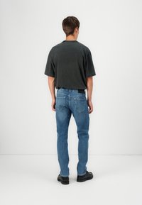 Camiseta oversize de color gris oscuro combinada con vaqueros ajustados azules. Los zapatos son negros. El fondo es blanco liso, resaltando el conjunto.