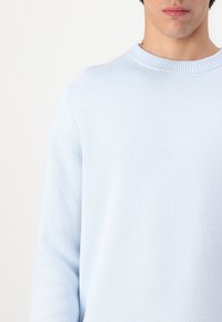 Light blue sweater made of soft knit fabric. Features a classic crew neck and long sleeves with a smooth texture.