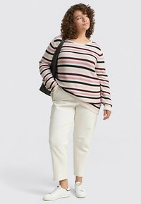 Langärmeliges, gestreiftes Oberteil in Pink, Schwarz und Weiß; lockere Passform. Kombiniert mit cremefarbenen, zulaufenden Hosen und weißen Sneakern.