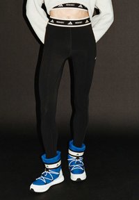 Svarta leggings med hög midja och vitt varumärkeslogotyp. Matchat med blå och vita sneakers i ankellängd med snördetaljer.