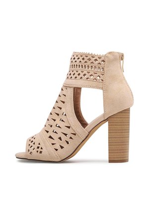 Sandale beige à bout ouvert avec un motif perforé, en cuir suédé texturé, et un talon épais rainuré. Fermeture éclair latérale.