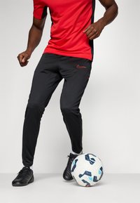 Rød sports T-shirt med sorte sidelapper, parret med sorte bukser med røde accenter. Sorte fodboldstøvler, hvid fodbold med blå og sorte detaljer.