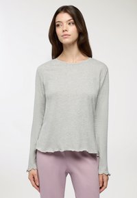 Maglia a maniche lunghe grigia realizzata in un tessuto morbido con scollatura rotonda e orli scallop, abbinata a pantaloni viola chiaro.