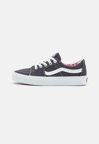Sneaker nera bassa con lacci bianchi, striscia bianca laterale e fodera interna a motivo floreale su sfondo bianco.