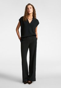 Top negro de cuello en V con mangas cortas, combinado con pantalones negros de cintura alta. Tela lisa con un ligero brillo y corte de pierna ancha.