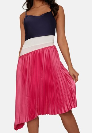 Jupe plissée en satin rose, avec un haut bleu marine et une taille blanche. L'ourlet asymétrique ajoute une forme dynamique. Texture lisse sur toute la surface.