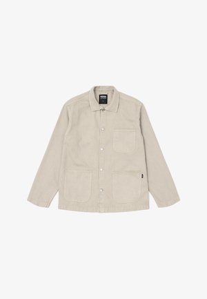 Světle béžová bunda vyrobená z bavlny, s knoflíkovým zapínáním vpředu, špičatým límcem a dvěma velkými předními kapsami s viditelnými švy.