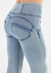 Jeans en denim bleu clair taille haute au design ajusté, avec des poches incurvées et des accessoires en métal argenté.