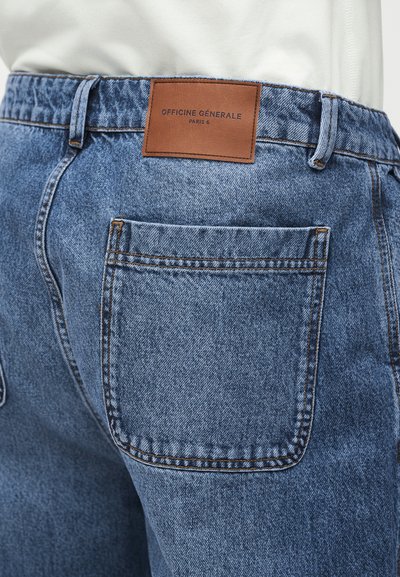 Πίσω όψη μπλε τζιν με δερμάτινη καφέ ετικέτα επιγραφόμενη "Officine Générale Paris 6" πάνω από τη δεξιά πίσω τσέπη.