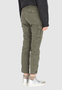 Olivově zelené cargo kalhoty s bočními kapsami, zúženými nohavicemi a nastavitelnými lemy, doplněné stříbrno-šedými teniskami s vysokým svrškem.