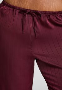 Pantalon en satin bourgogne avec des rayures verticales, doté d'une taille élastique et d'un cordon de serrage. Texture lisse, design ajusté.