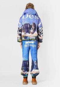 Chaqueta acolchada en azul con estampado multicolor de montañas y cuello extragrande; pantalones a juego con diseño similar y detalles gráficos de texto.