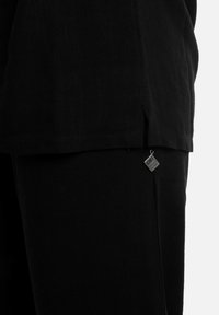 Zwarte cropped top met een rechte zoom, een textuurstof en een klein zilveren label bevestigd aan de zijnaad.