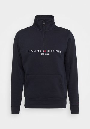 Granatowy pulower z zamek błyskawicznym i stójką, z logo "TOMMY HILFIGER" oraz napisem "EST. 1985" w kolorze białym. Wykonany z miękkiego materiału, z kieszenią z przodu.
