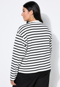 Maglione a righe bianche e nere con maniche lunghe, vestibilità ampia, scollatura rotonda e spalle scese, abbinato a pantaloni neri.
