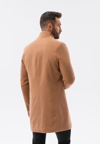 Cappotto beige con colletto alto, vestibilità sartoriale e maniche lunghe. Realizzato in tessuto liscio e di peso medio. Cuciture pulite e design minimal.