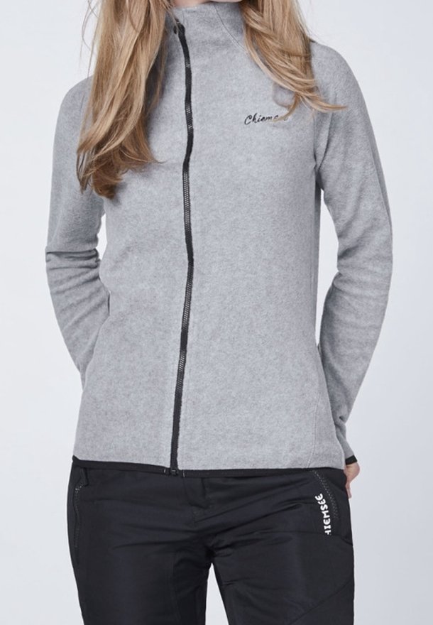 Szara polarowa kurtka zapinana na zamek z wysokim kołnierzem, z czarnym zamkiem błyskawicznym i haftowanym logo. Połączona z czarnymi spodniami z białym nadrukiem.