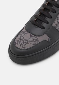 Černé tenisky s koženým svrškem a textilním panelem s geometrickým vzorem, kulaté tkaničky a gumová podrážka.