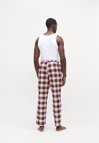 Pantalones de cuadros rojos y blancos con cintura elástica, combinados con una sencilla camiseta sin mangas blanca. El modelo está descalzo y de espaldas.