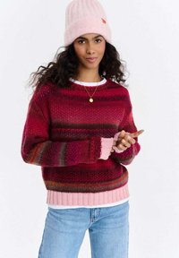 Sweter dziergany w odcieniach czerwieni i różu z paskowym wzorem, z prążkowanym obszyciem i mankietami. W komplecie z jasnoróżową czapką beanie.