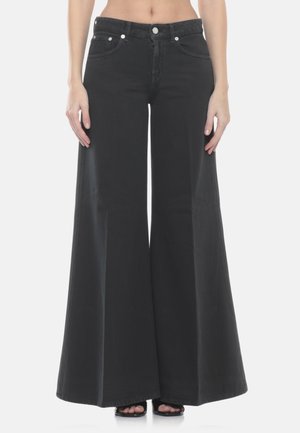 Jeans neri a gamba larga indossati da una persona in piedi, con bottone e tasche in vista, e scarpe nere con tacco aperto e punta scoperta visibili.