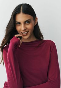 Dlhý rukáv bordového trička s jemnou textúrou, širokým výstrihom a priliehavými rukávmi, vytvárajúc relaxovaný siluetu.