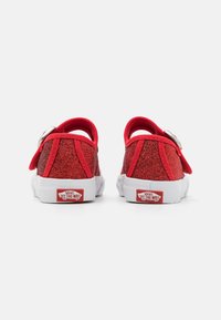 Raudoni blizgūs sportbačiai su minkštu viršumi, balta guma padas ir galinė kilpa. Įrengtas Velcro dirželis ir Vans logotipas ant kulno.
