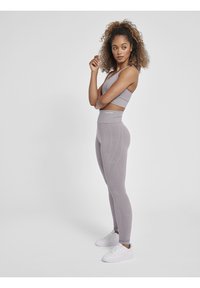 Lys grå sports-bh og leggings lavet af tekstureret stof, med høj talje og subtile designs. Modellen har hvide sneakers på.