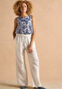 Lainetehitatud sinine mustriga tank top koos valgete paeltega laia lõikega pükste ja siniste kontsadega tekstuurilisel pinnal.