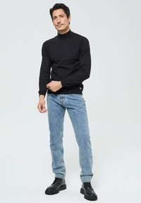 Pull à col roulé noir, au design ajusté, associé à un jean bleu clair. Position de face, portant des bottes noires à lacets. Simple et décontracté.