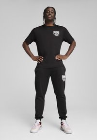 Mustvalge lühikeste varrukatega t-särk valge logoga, koos mustade treeningpükste ja sama logoga ning valgete spordijalatsitega.